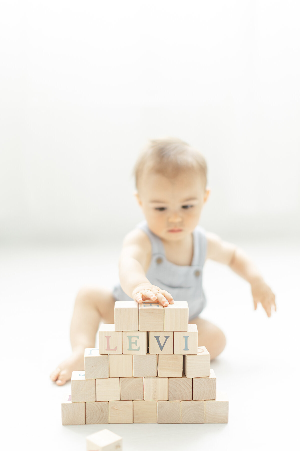 A baby boy playing on a Dallas photography floor with wooden blocks as he stacks them on top of each other.