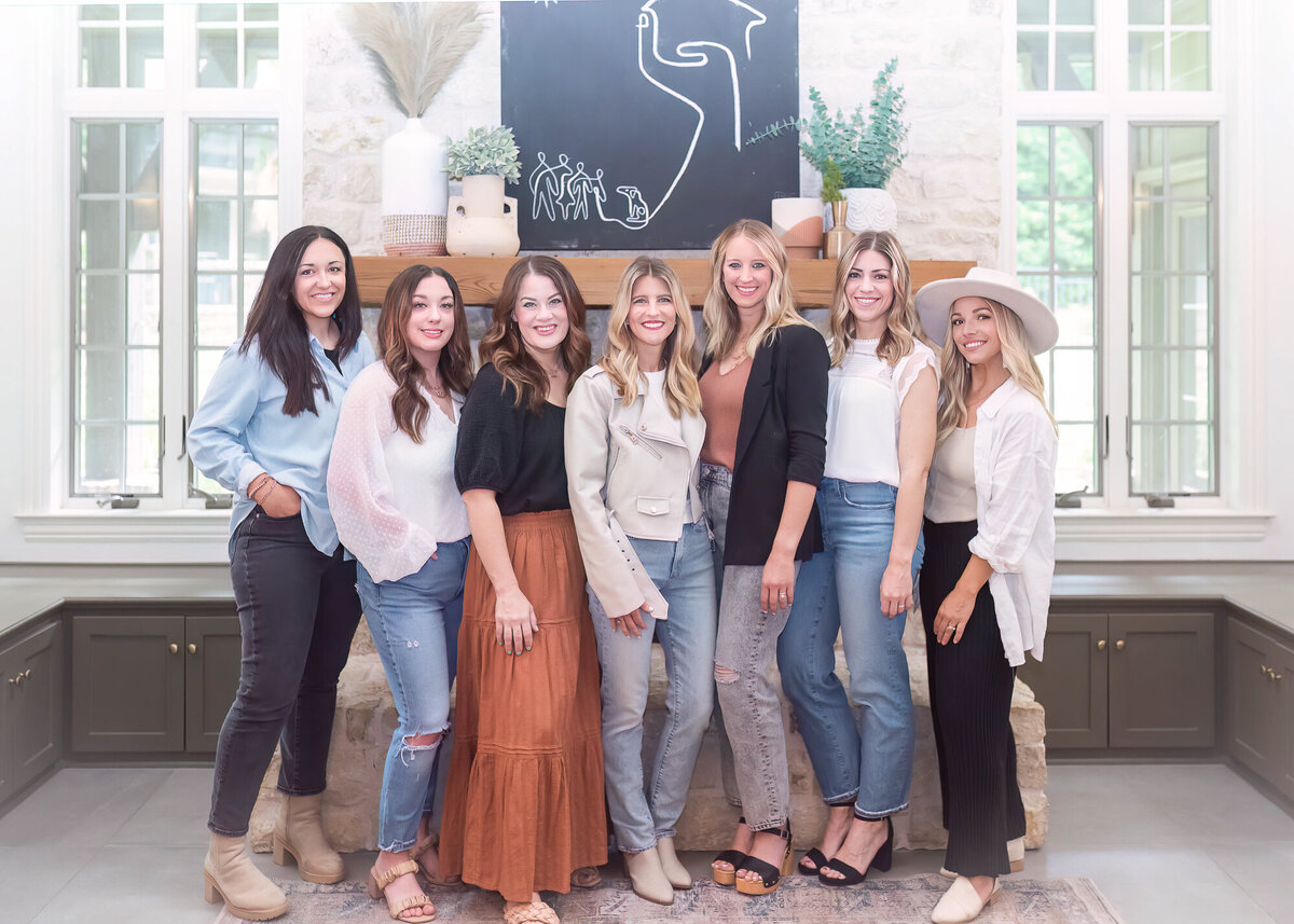 interior design team of women standing in front of a fireplace smiling
