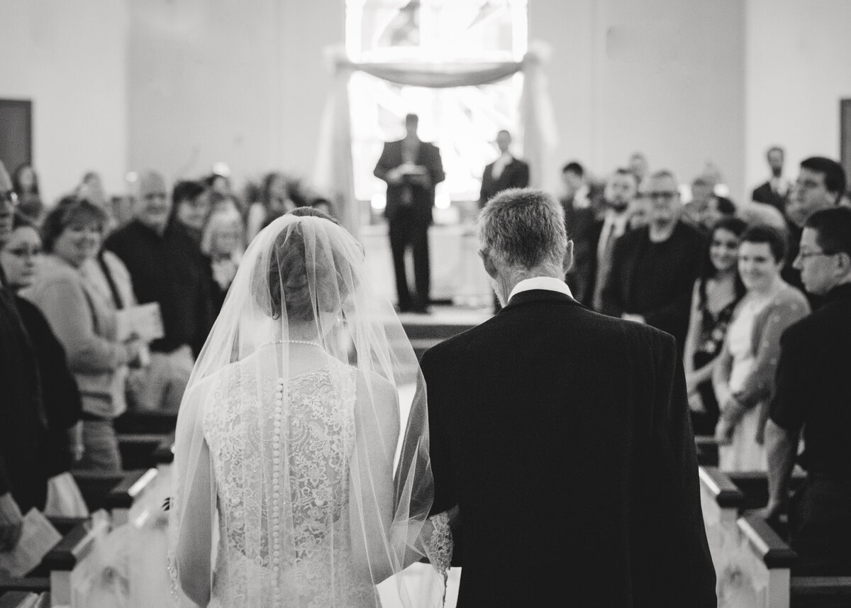 bride walks down aisle escorted by her father with guests standing