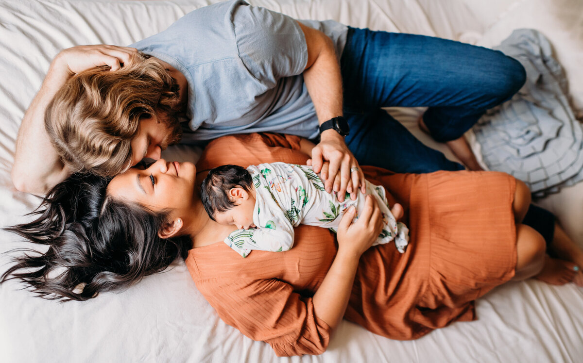 Newborn Photographer, Mom and dad laying down and kissing with baby girl on their chest.