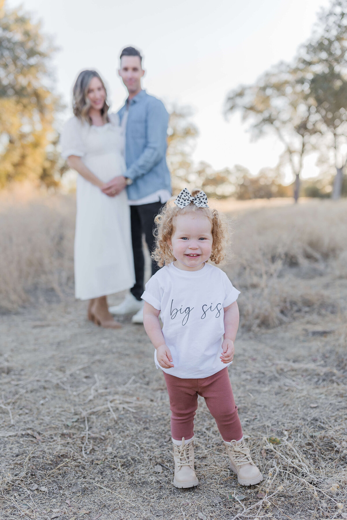 couple standing in the back while toddler is in the front wearing big sister t-shirt  during pregnancy announcement photos