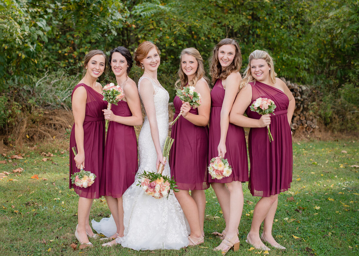 bride with bridesmaids holding flowers in maroon short dresses