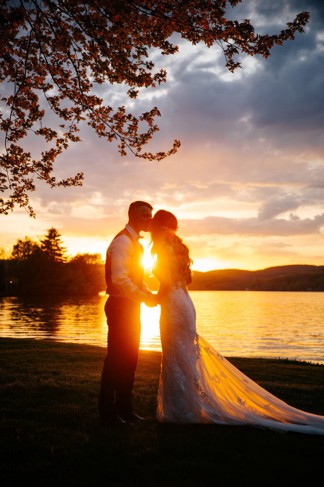 sunset silhouette bride and groom kissing in front of water at lake bomoseen lodge wedding