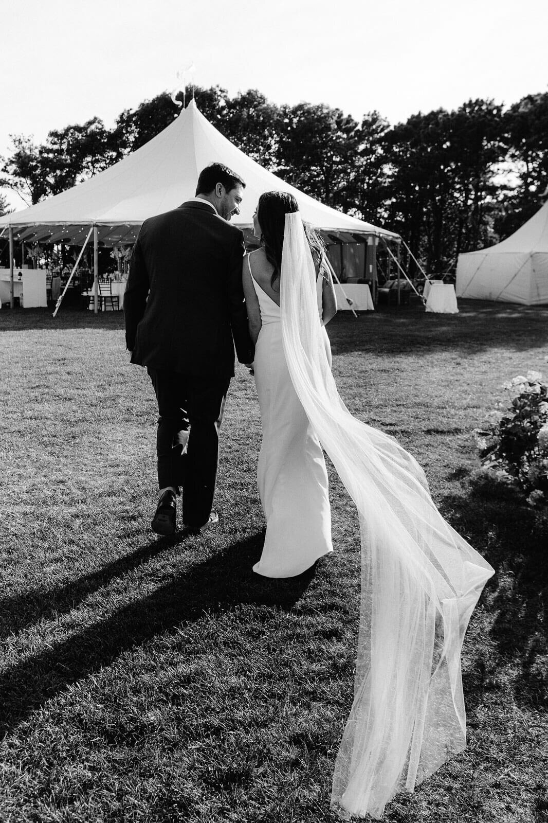 Black and white photo of the bride and the groom walking towards the Cape Cod Summer Tent in MA, after the wedding ceremony.