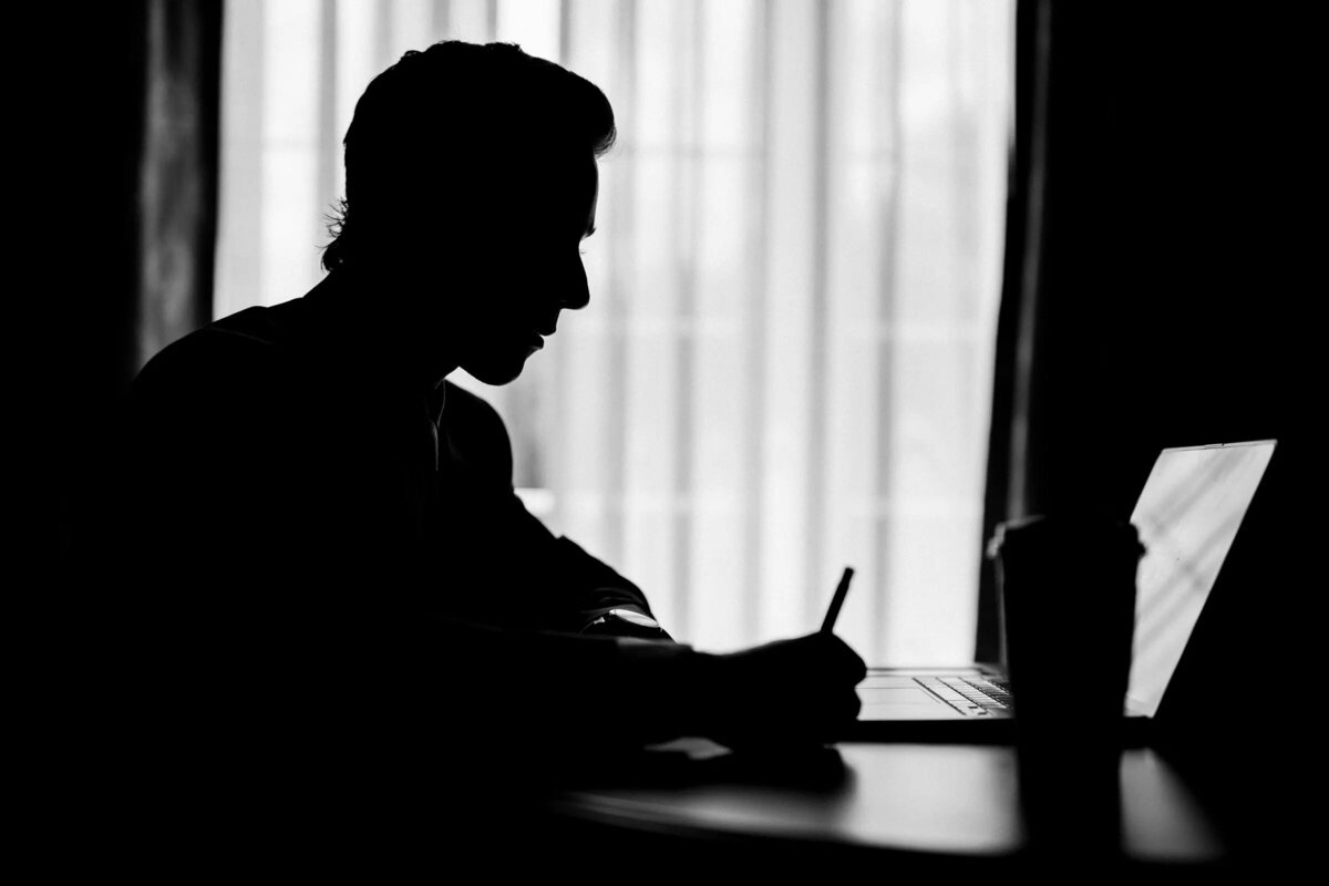 A silhouette of a man writing at a desk, with the outline of his profile illuminated against the light coming from a window.