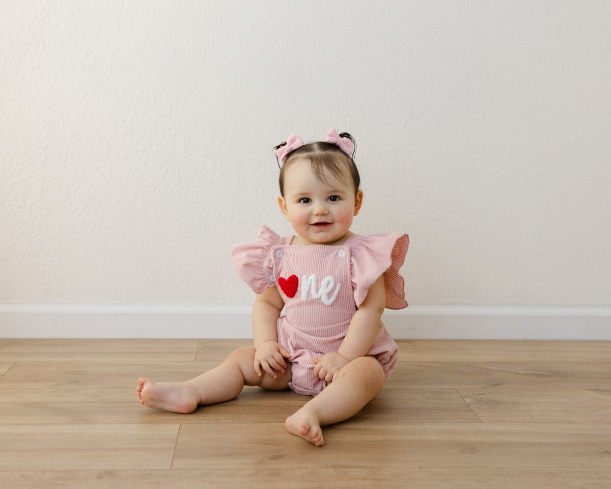 Pink romper, sweet smile, and a heart full of birthday joy. Captured by Yucaipa cake smash photographer Kaitlyn Dawn Photography.