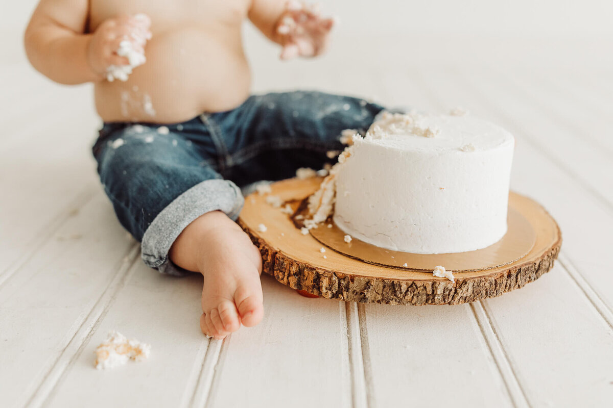 Details image of baby boys cake smashed toes with his cake sitting on a wooden block in studio.