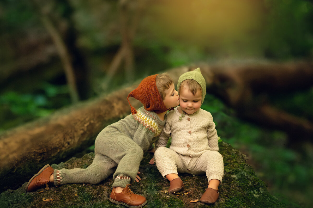 An young boy is photographed kissing his little brother on the cheek in a middle-earth inspired fantasy setting.