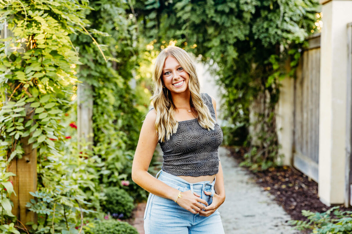 young lady with her hair down, holding her thumbs in her belt loops as she poses in a gorgeous garden in Green Bay