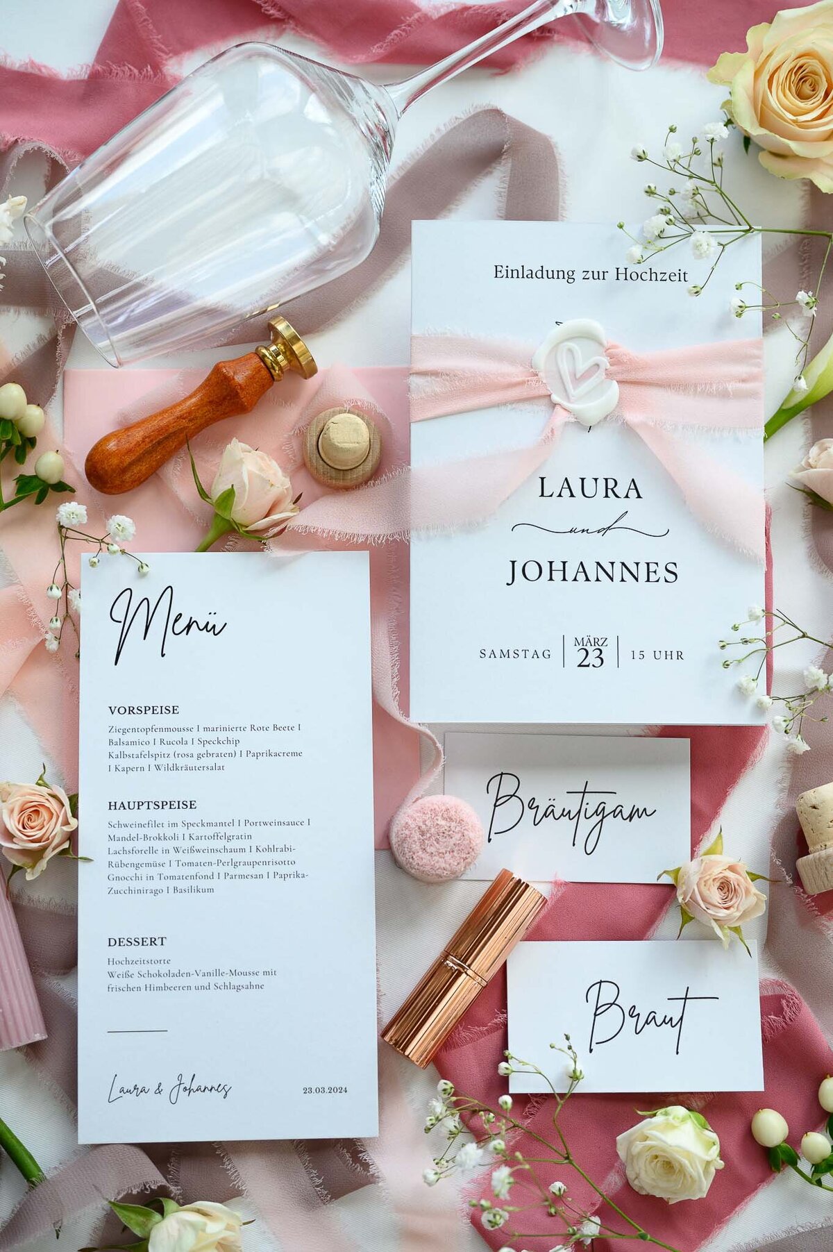 Papeterie einer Hochzeit angerichtet mit Blumen, Lippenstift und Dekoband