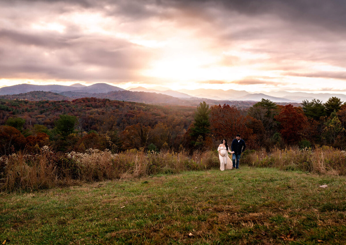 An expecting couple dance and laugh on a mountain top near Asheville NC