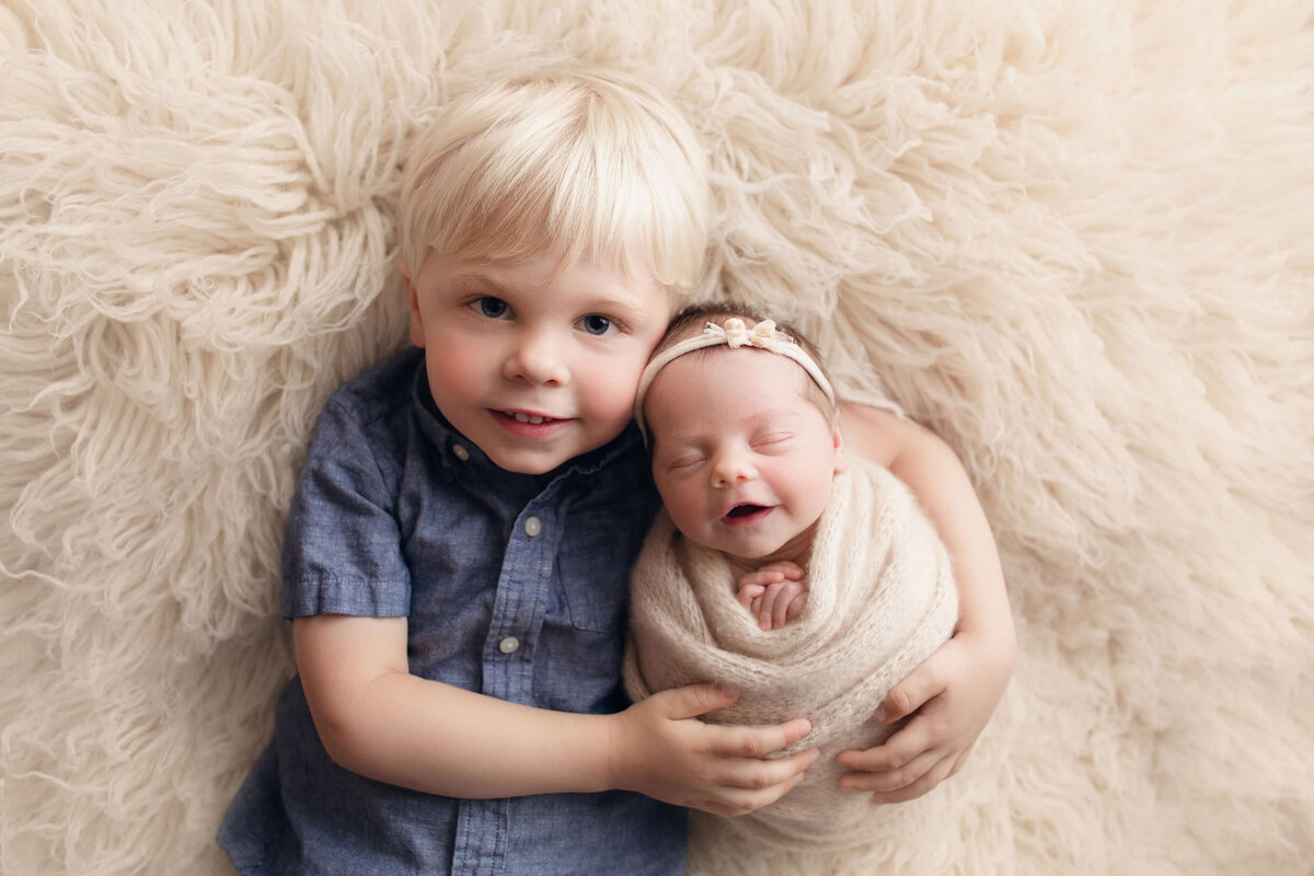 boy and newborn girl snuggled on white blanket