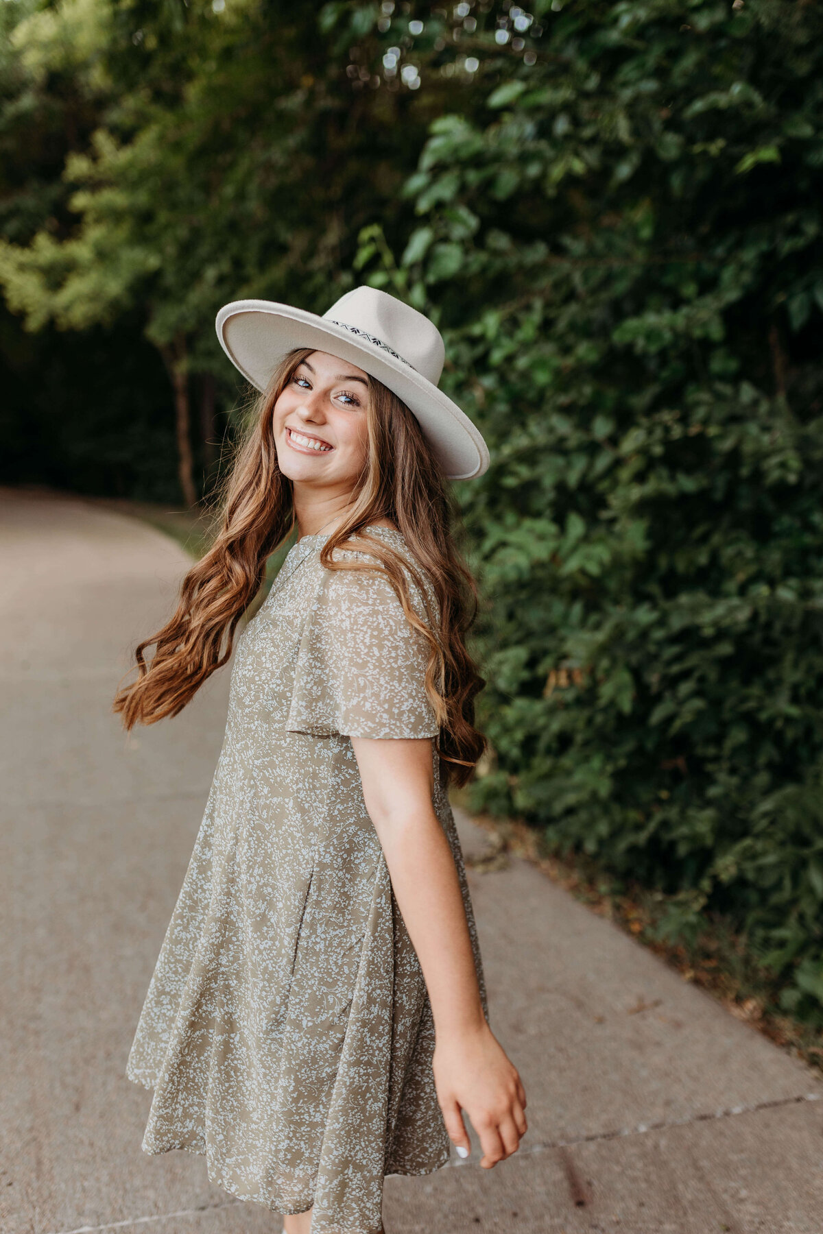 Senior girl wearing a dress and hat  twirls along  a path in Nebraska