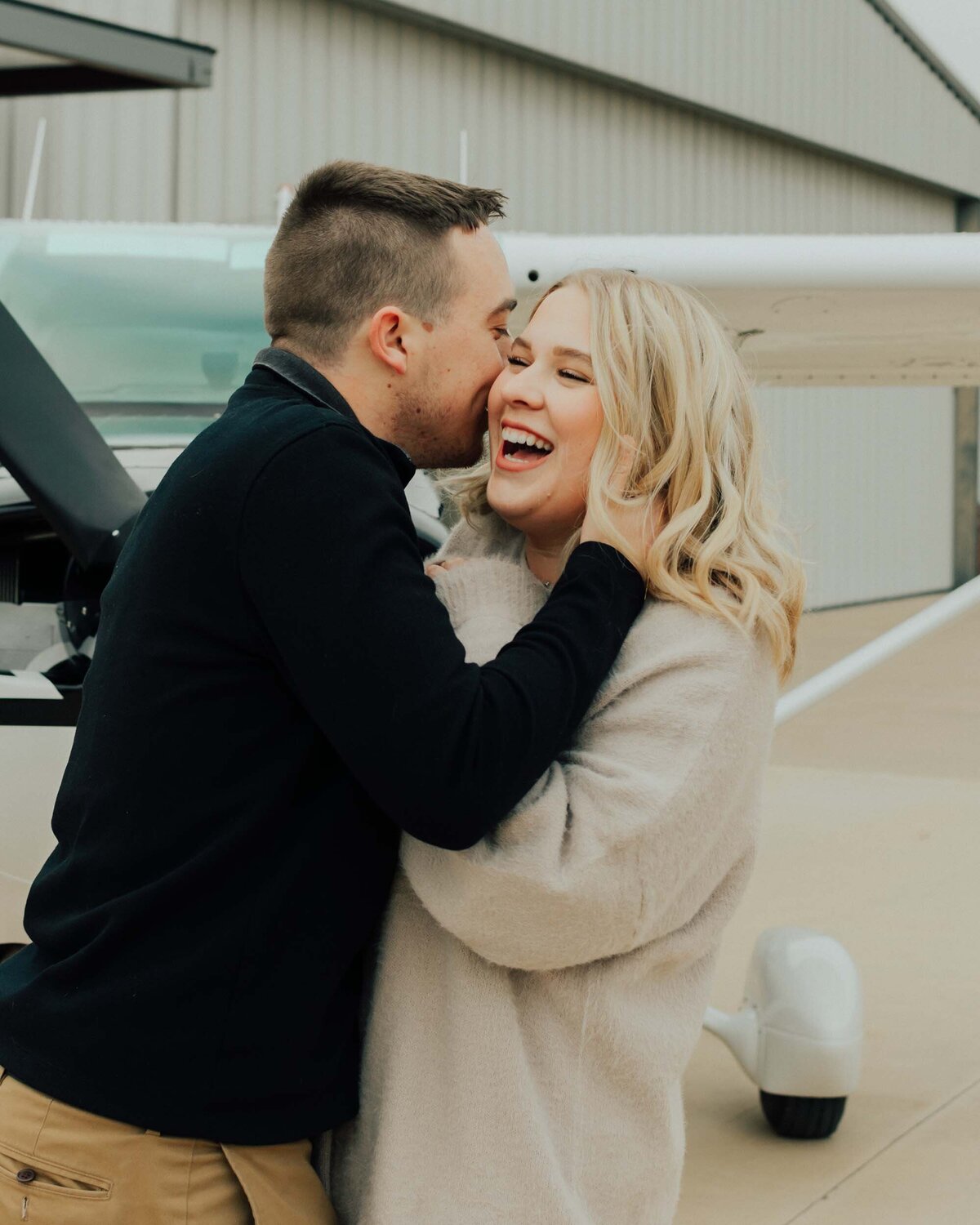 Maddie Rae Photography couple standing face to face in front of a small airplane. he is whispering in her ear and she is laughing