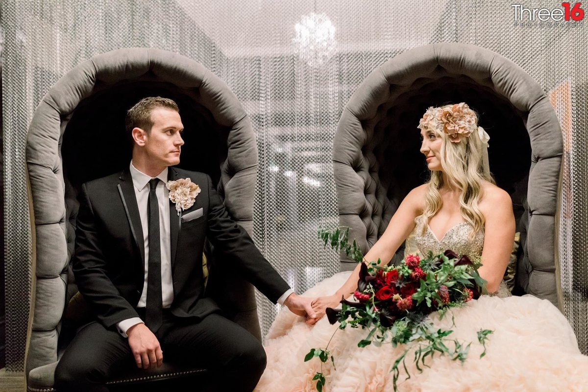 Bride and Groom stare at each other and hold hands sitting in separate chairs with chains as walls behind them
