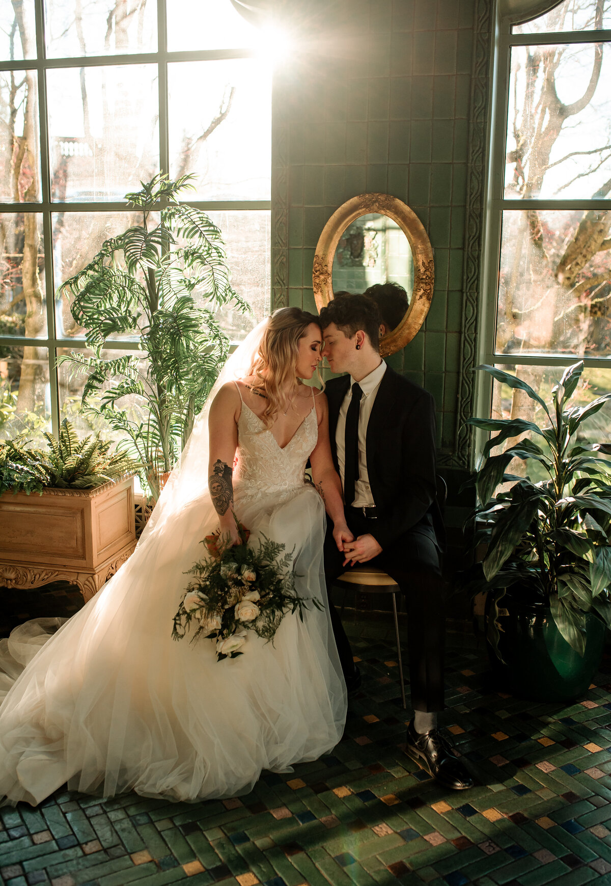 Bride and groom sitting down holding one hand, foreheads touching and eyes closed. Sunset and in a greenery setting.