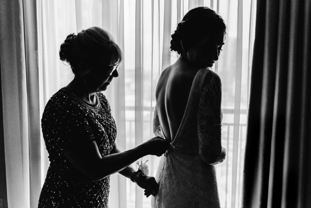 Mom helps zip of daughters wedding dress with moody light