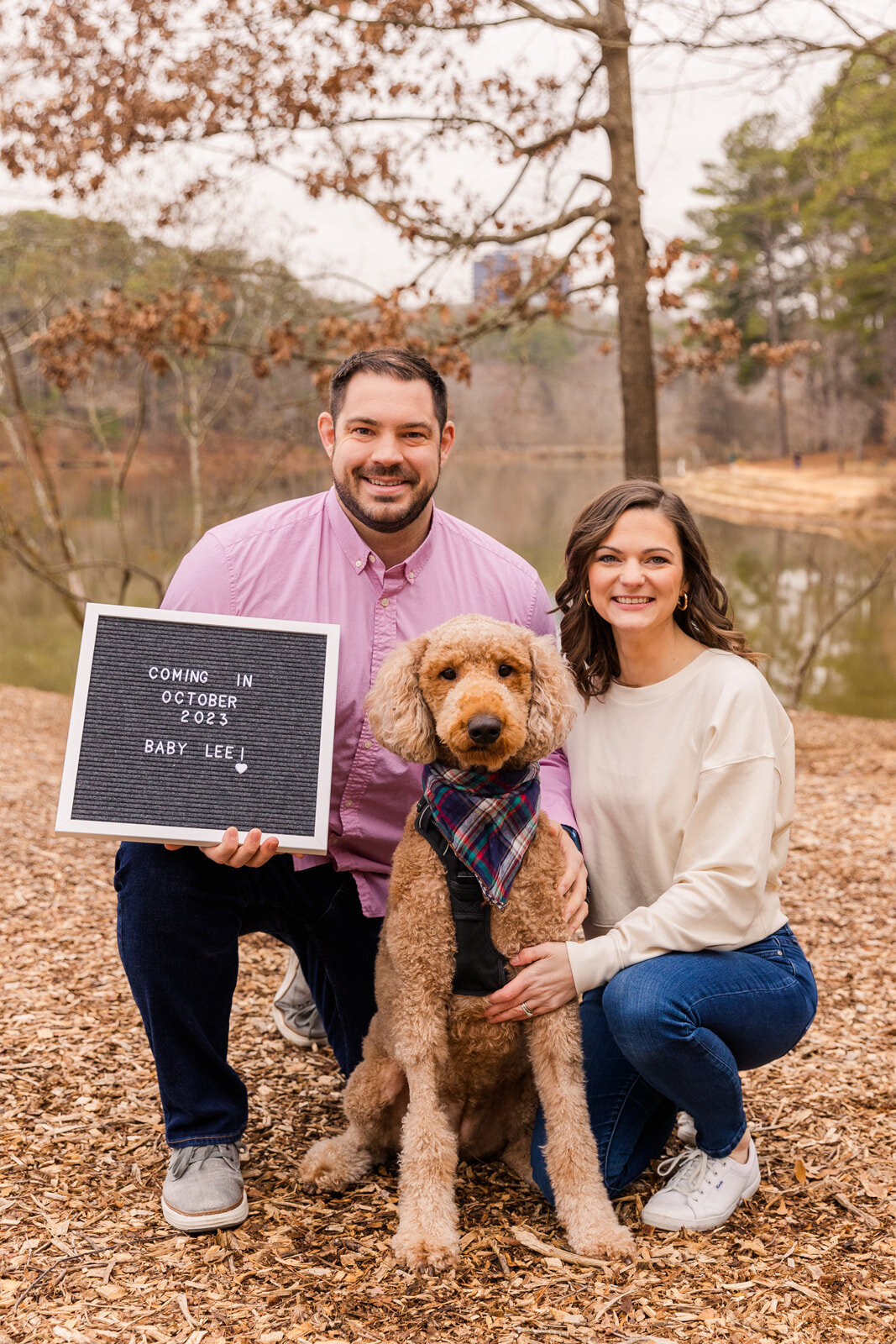 Couple with dog announcing pregnancy with  message on a board during winter byin a park near a lake Atlanta by Laure Photography