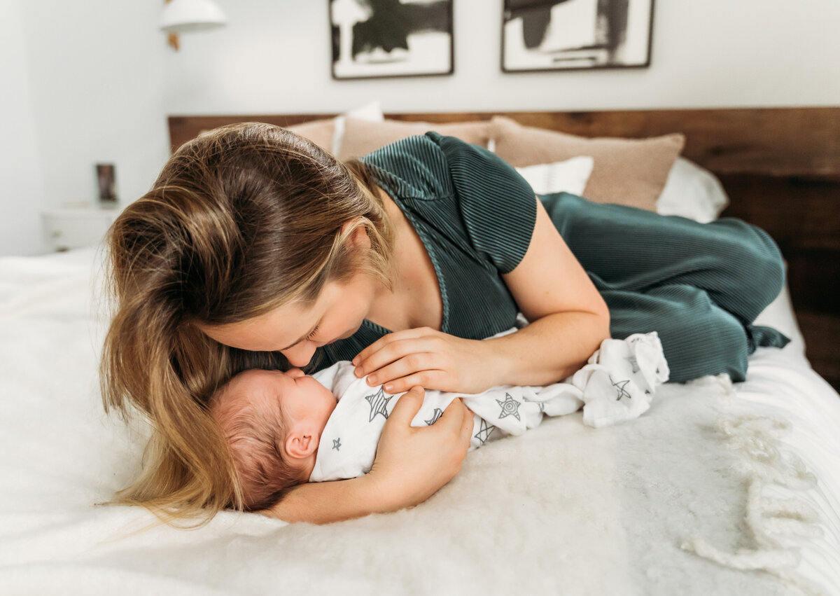 Newborn Photographer, a mom leans over her baby that lays on her bed, she dotes on baby