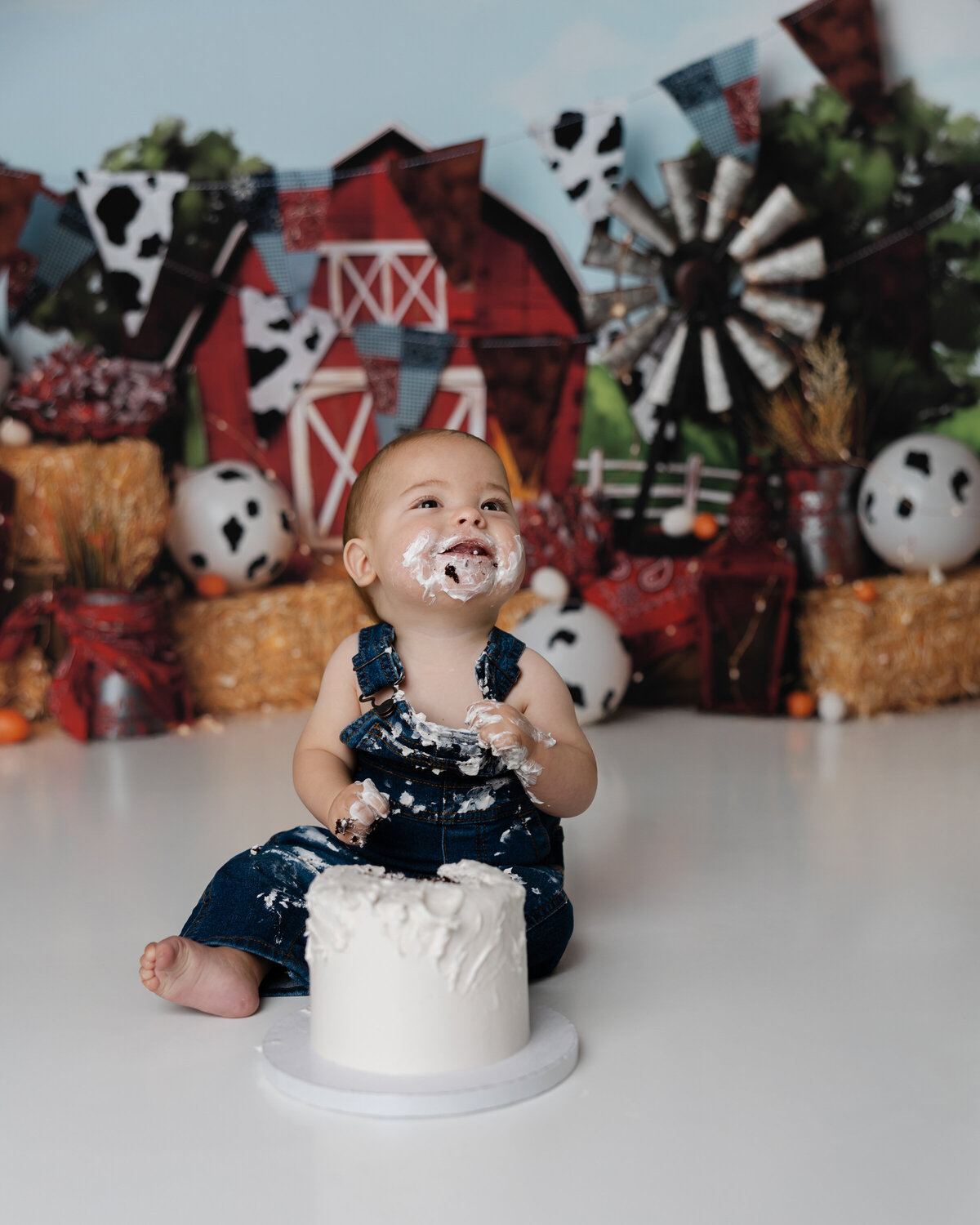 Barnyard birthday celebration with baby boy smiling mid-cake smash, surrounded by themed props and hay. Photograph by Yucaipa cake smash photographer Kaitlyn Dawn Photography.