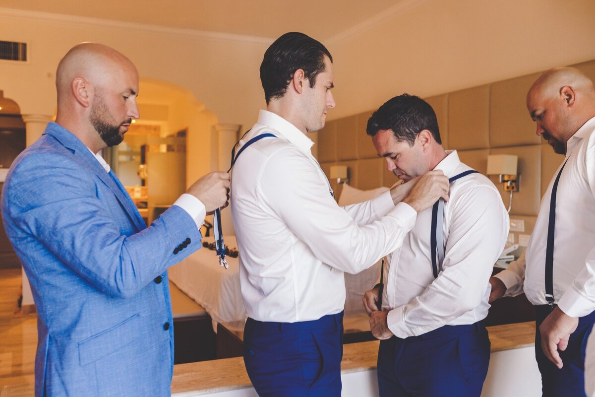 Grooms and groomsmen adjusting suspenders before wedding in Riviera Maya