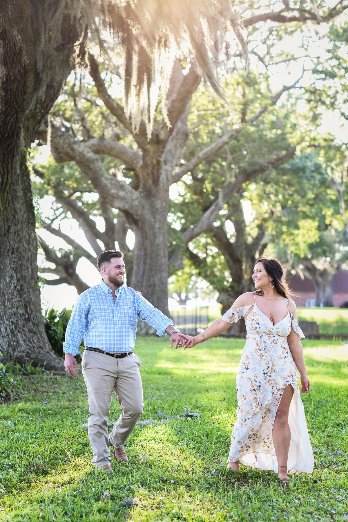 Beautiful Mississippi Engagement Photography: couple walks holding hands under oaks with spanish moss in Ocean Springs, MS