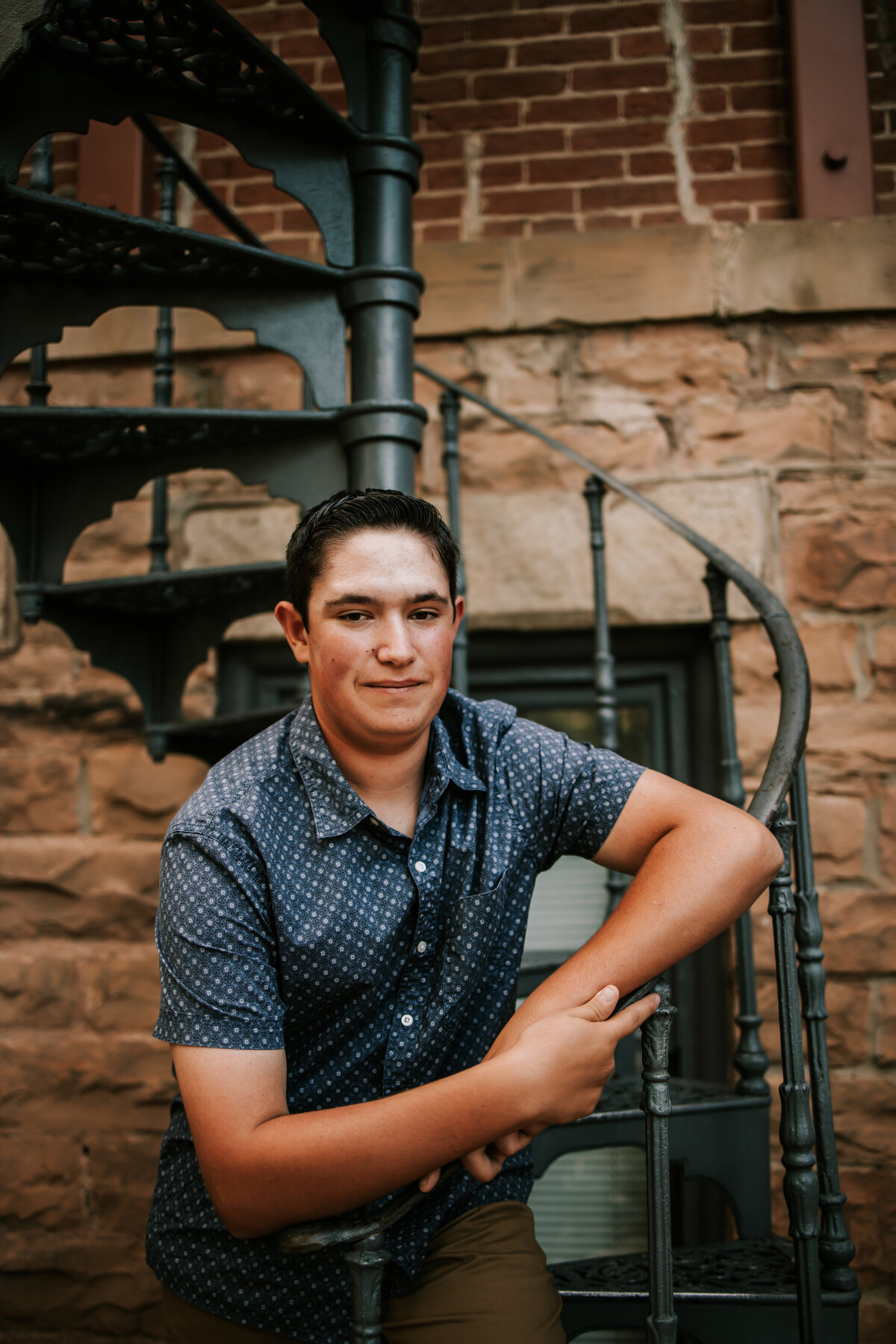 senior boy in blue button up leans against spiral staircase in boulder colorado for senior phtoos