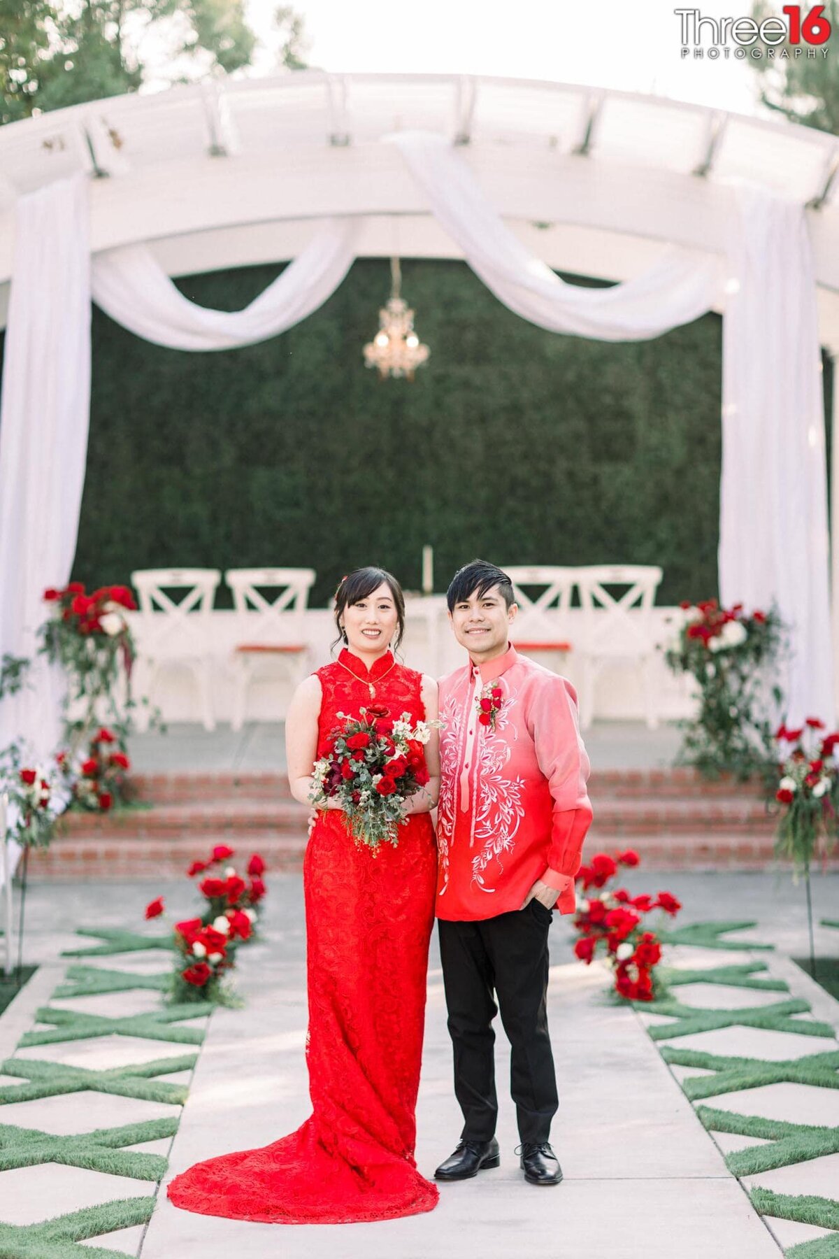 Bride and Groom wearing red attire pose together on the aisle