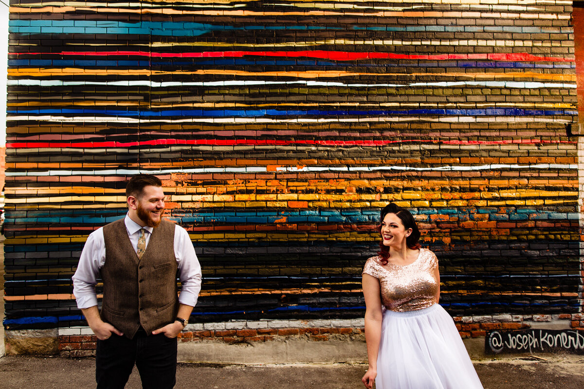 Classy Downtown Detroit Engagement photo of couple standing in front of a colorful wall laughing with each other. Photo By Adore Wedding Photography. Toledo Wedding Photographers