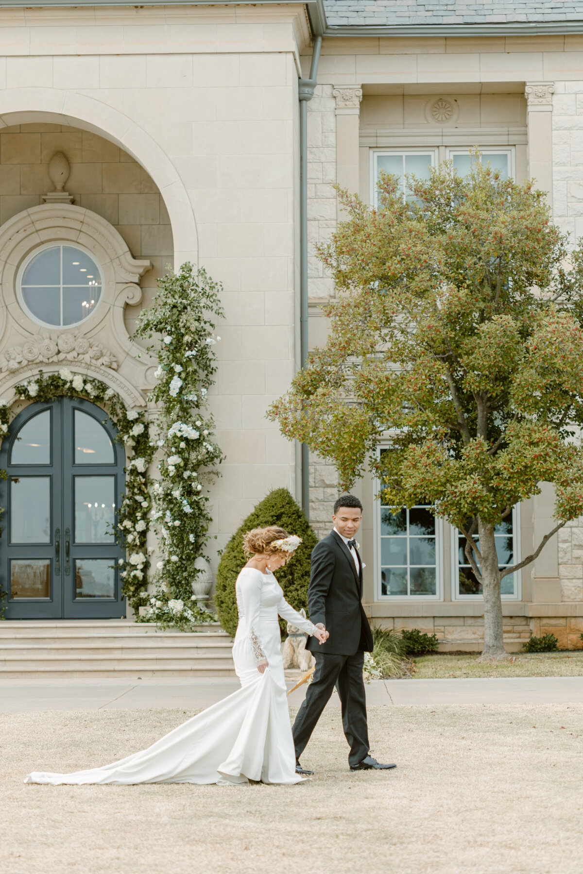 Bride and groom hold hands and walk outside their wedding venue covered in flowers