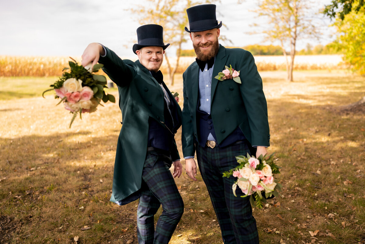 Grooms smile and hold flowers.