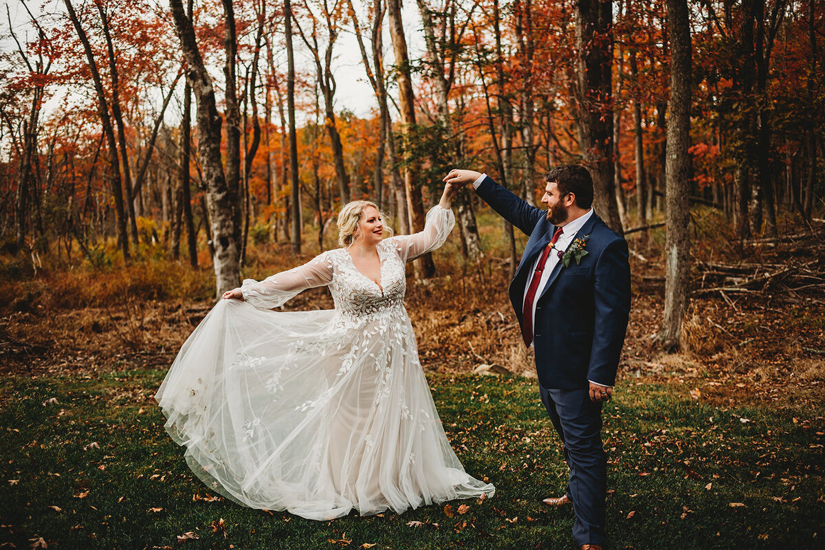 Fall wedding in Maryland with bride and groom dancing together in a field with autumn trees in the distance captured by Baltimore wedding photographers