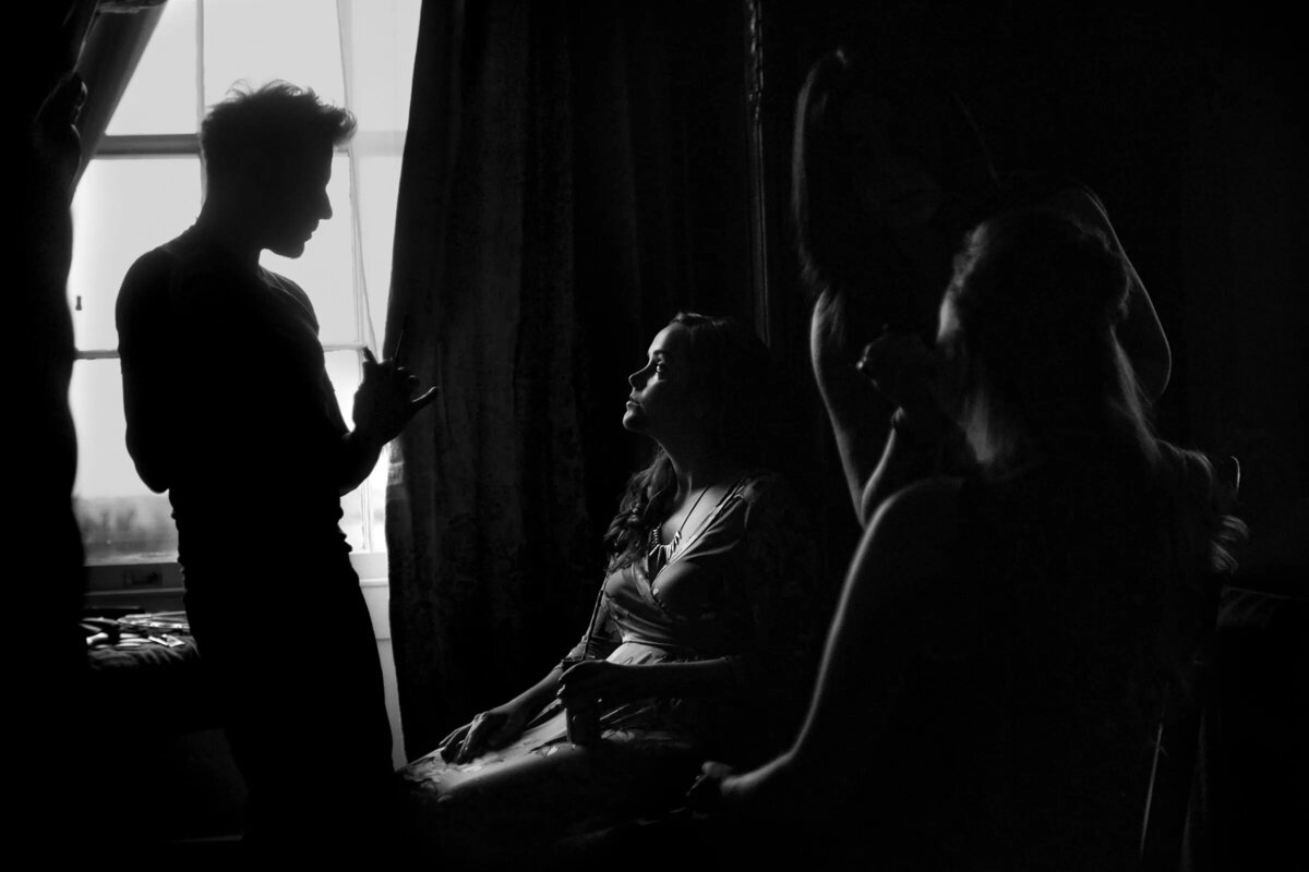 Silhouetted figures in a dimly lit room during bridal preparations