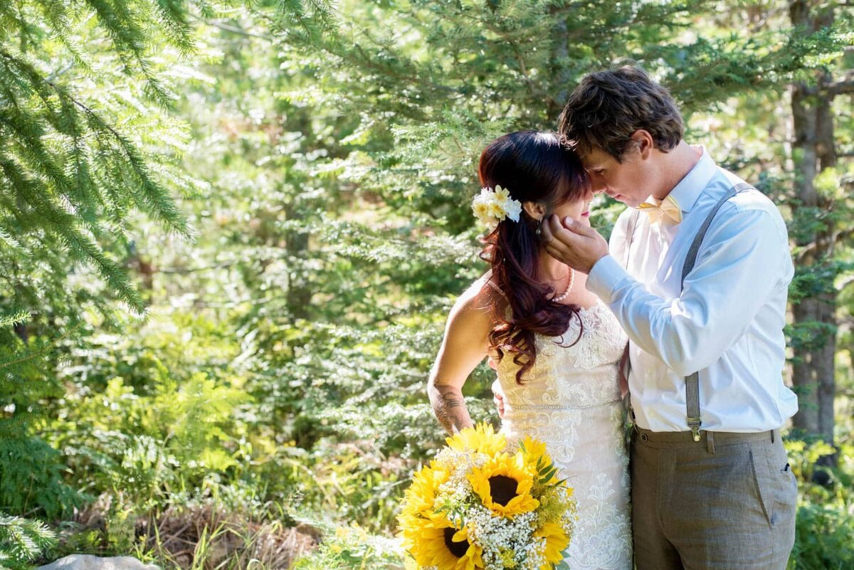 a groom holds a brides face close and she is holding a sunflower bouquet