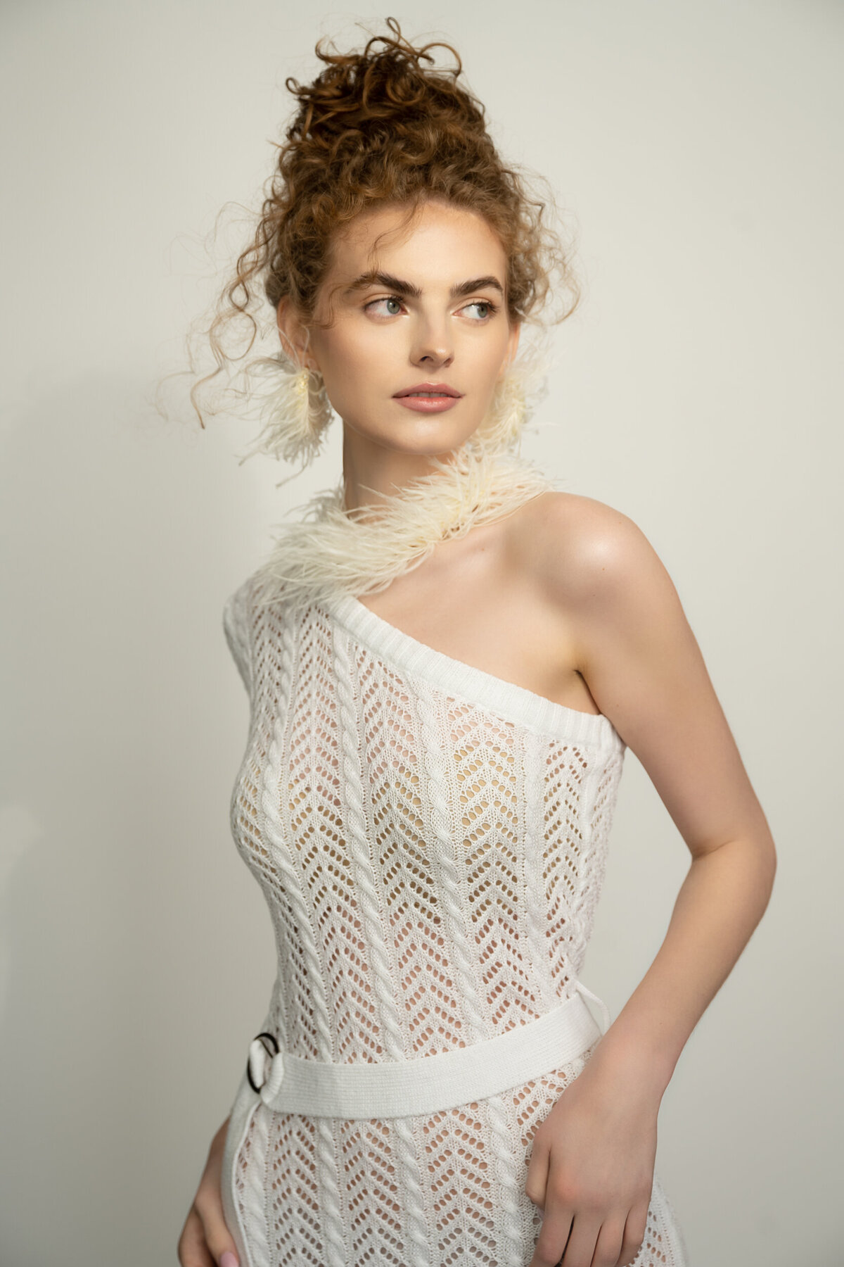 young woman with curly red hair wearing a white one sleeve dress