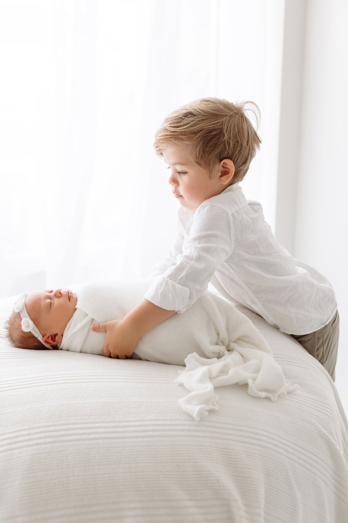 toddler trying to pick up newborn sister