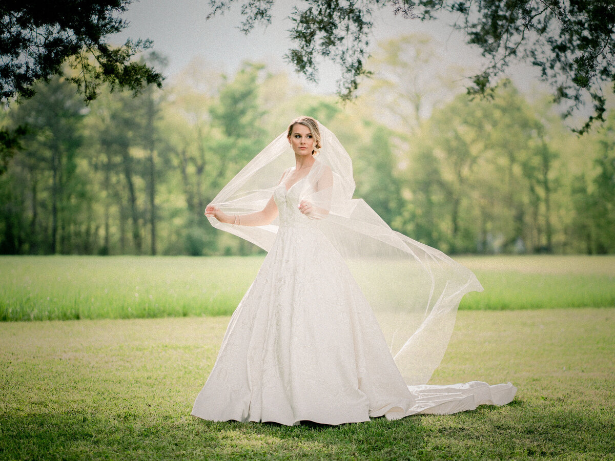 A bride standing in a field with her veil flowing around her