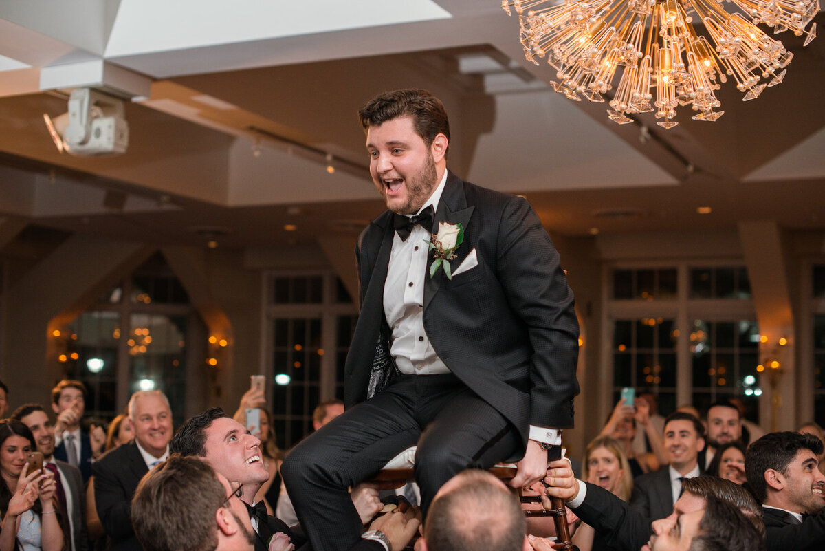 groom on a chair during the horah at Heritage Club at Bethpage