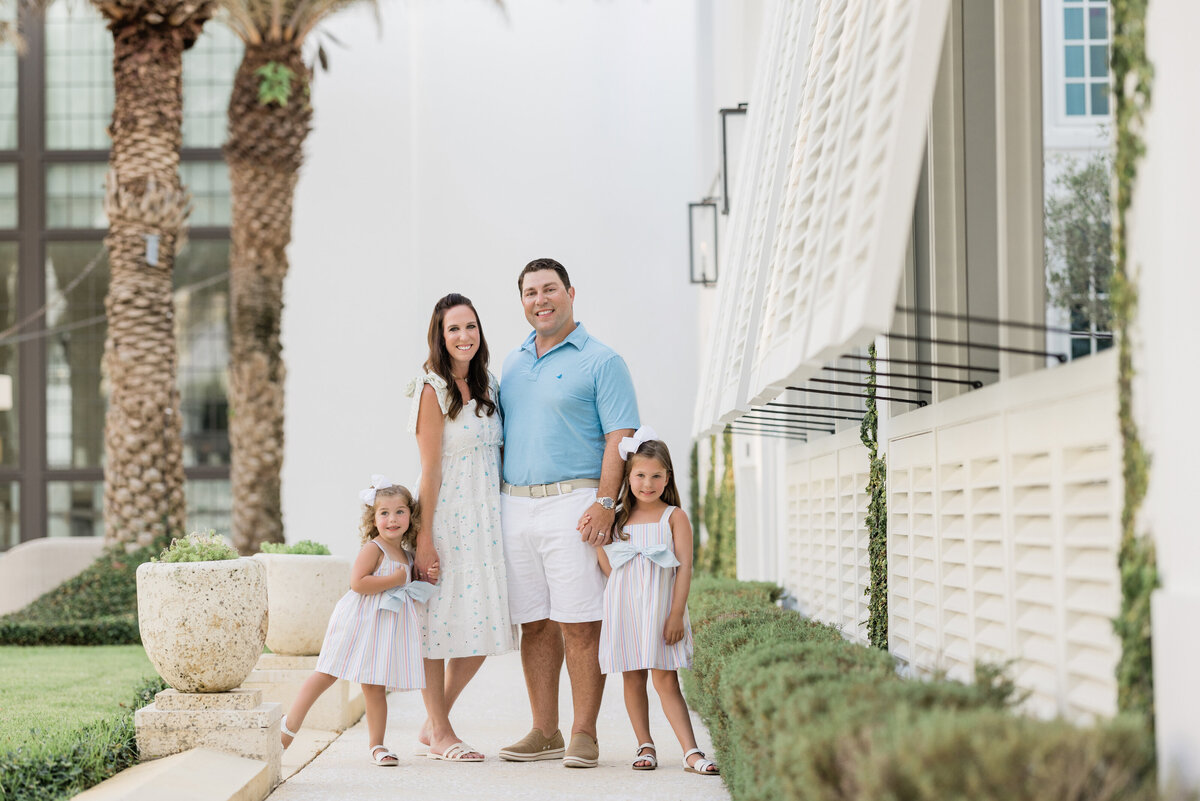 Two parents holding the hands of their children while standing on a sidewalk