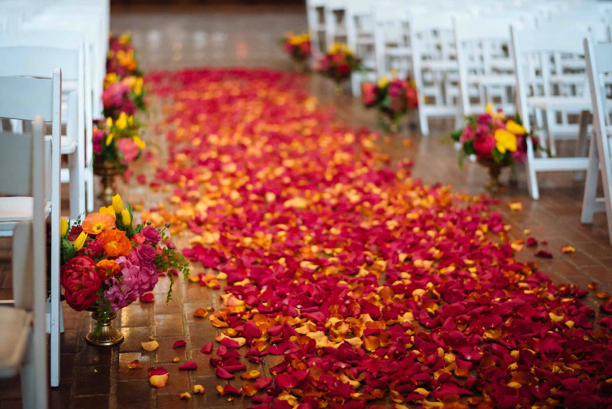 A mix of hot pink and orange rose petals cover the aisle for our bright indian wedding!