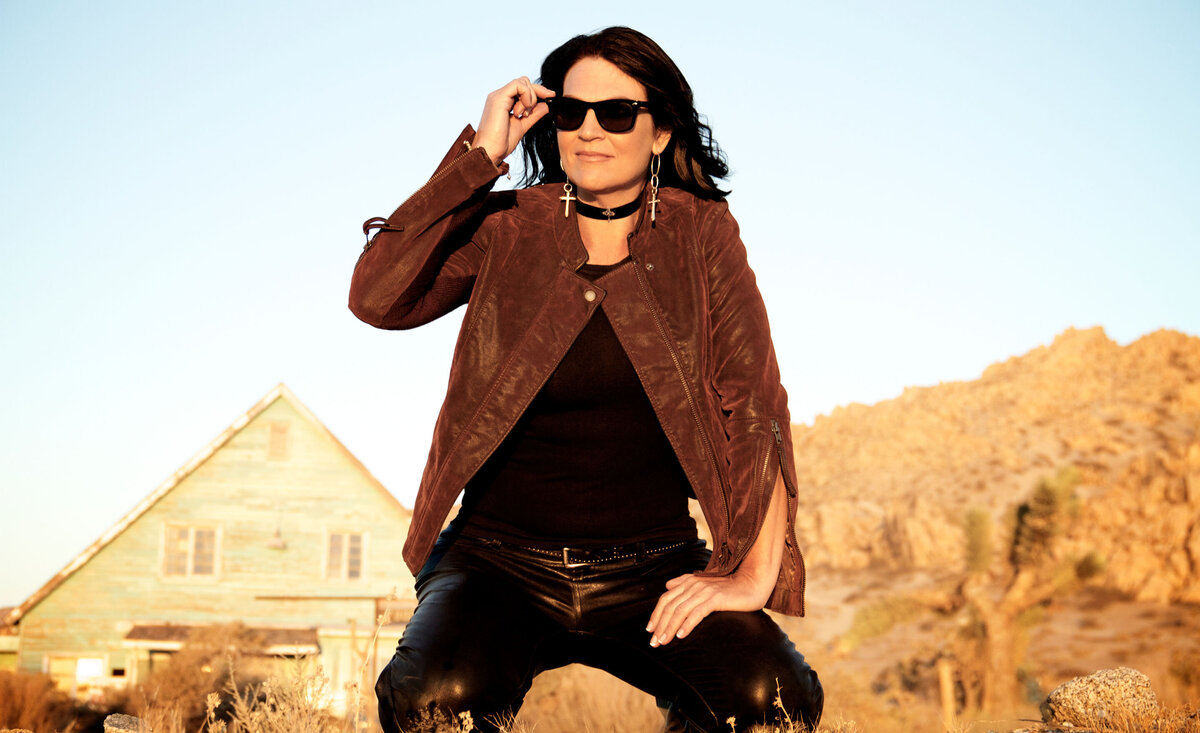 Country musician portrait Leslie Cours Mather taking off sunglasses kneeling down old desert motel behind