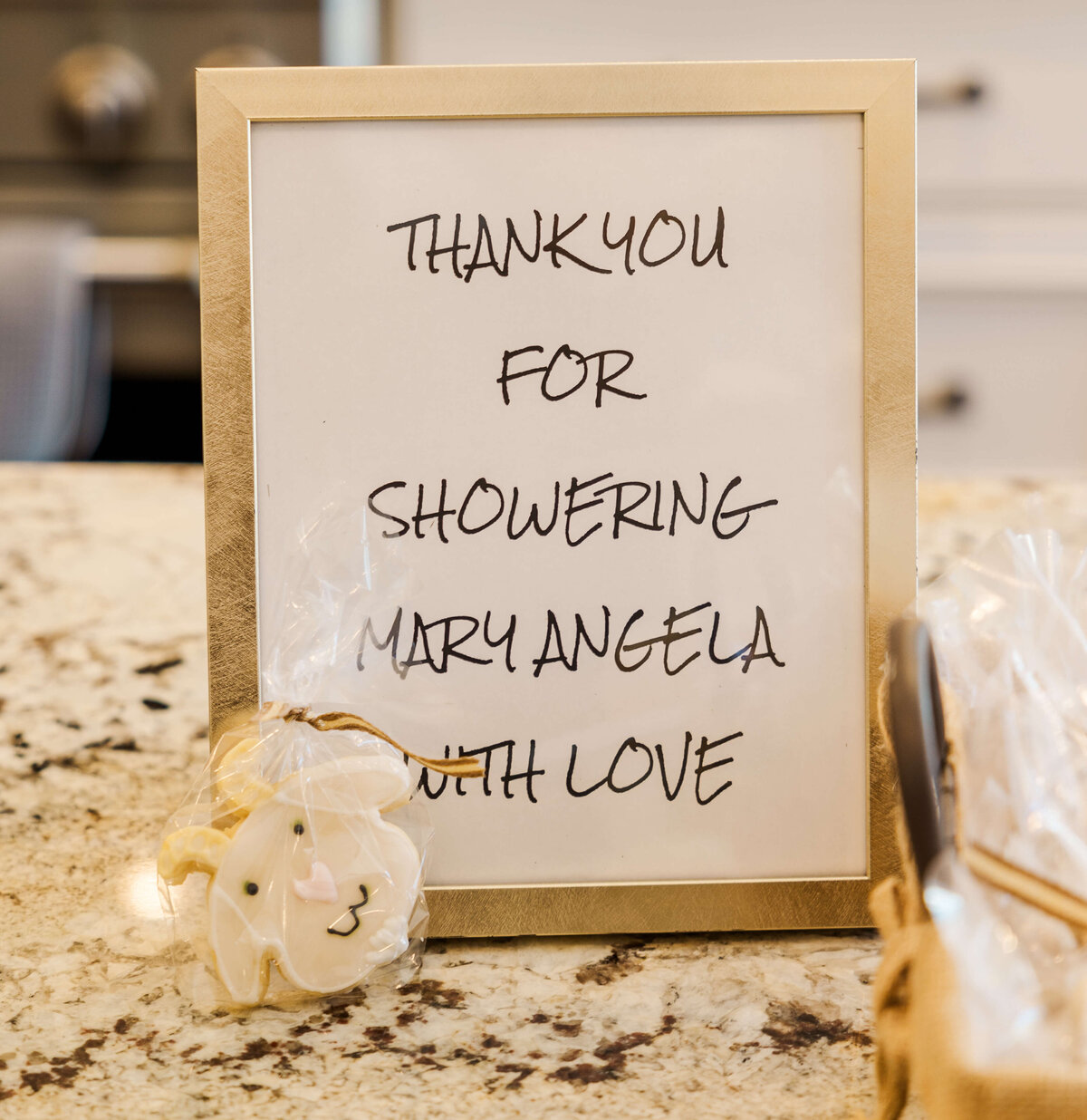 A framed sign on the counter reads, "Thank you for showering Mary Angela with love." Capturing this special moment, an event photographer in Fayetteville, NC preserves these heartfelt memories. Beside it is a cookie shaped like a baby's face wrapped in clear plastic.