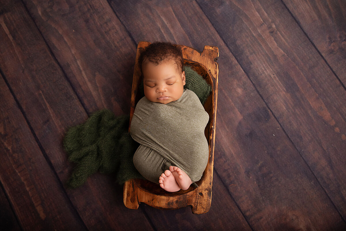 newborn baby in wood trench bowl with toes peeking