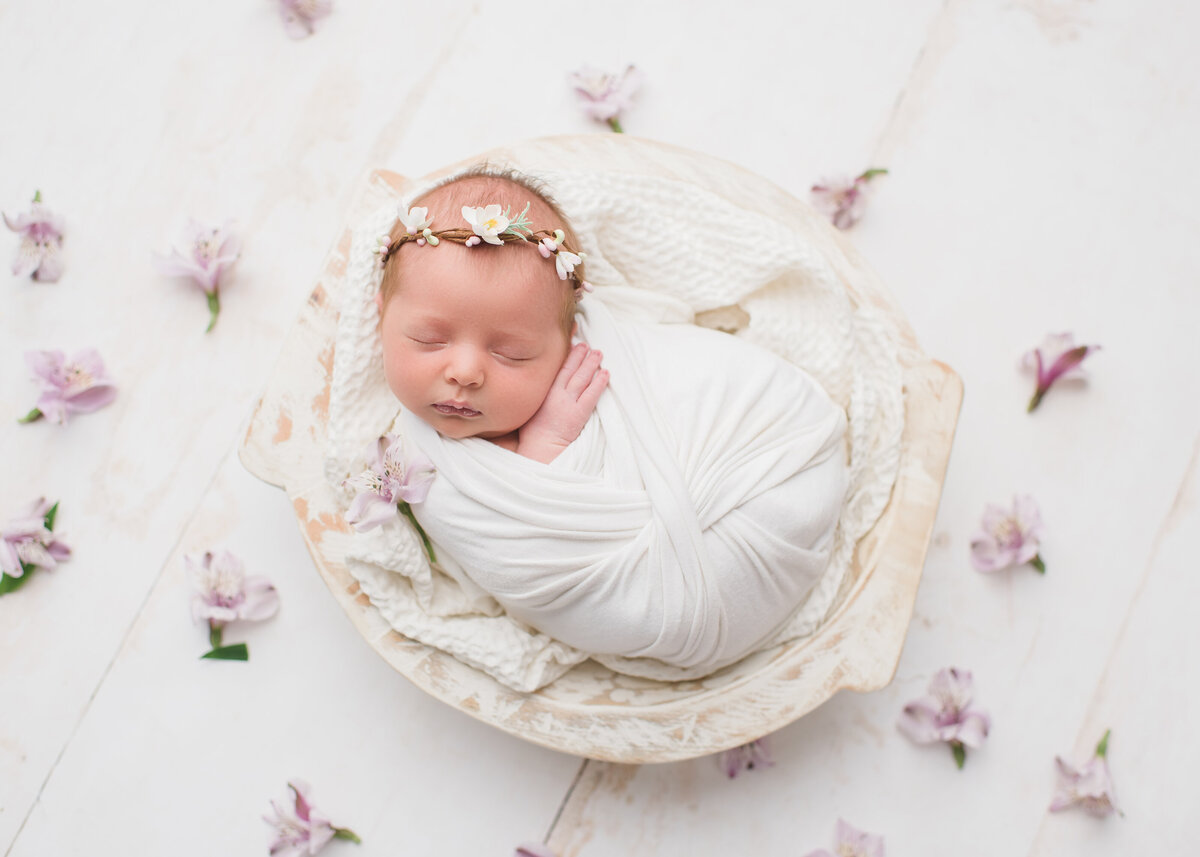 newborn with flowers around a white backdrop