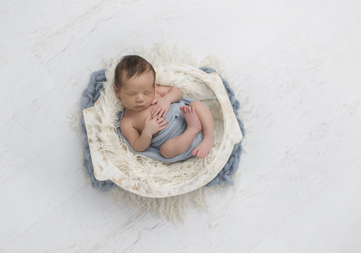 newborn laying down in a basket with a baby blue blanket and white backdrop