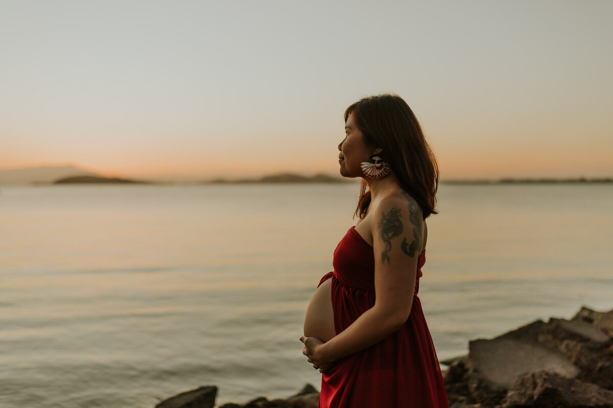 Blue hour maternity portrait of mom in red dress looking out toward the San Francisco bay