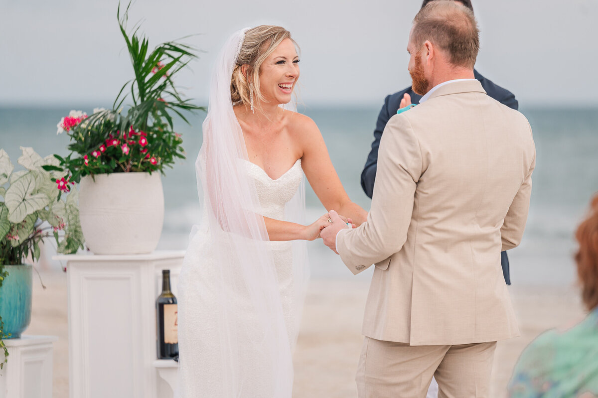 A laughing couple holding hands during their wedding ceremony at Atlantic Beach by Raleigh wedding photographer, JoLynn Photography