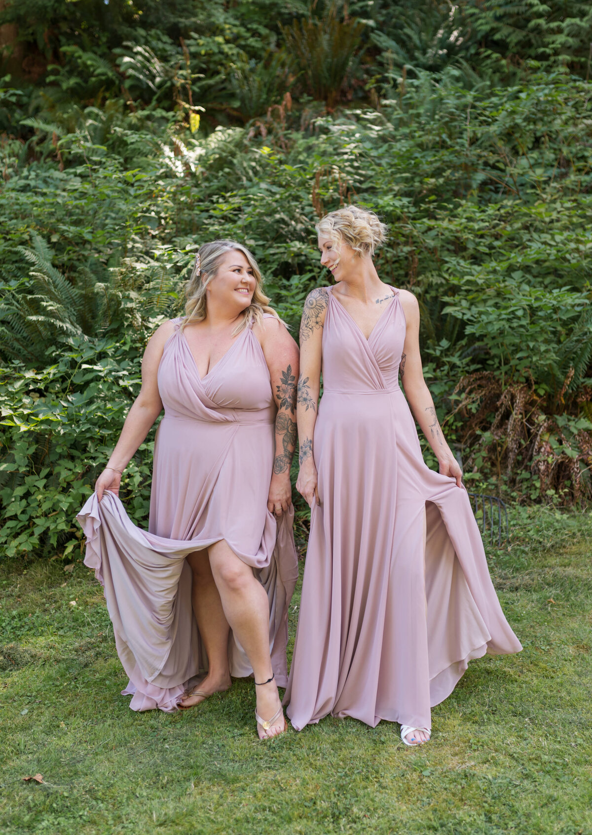 Bridesmaids pose on friends wedding day, girls are in pink looking at each other one hand on their pink bridesmaid dresses. 