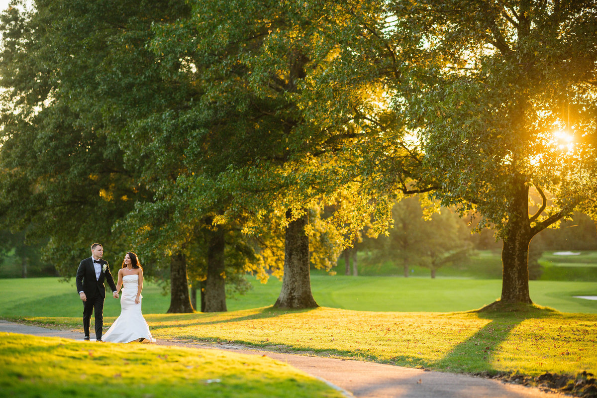 bride and groom walking on the cart path and holding hands at The Muttontown Club