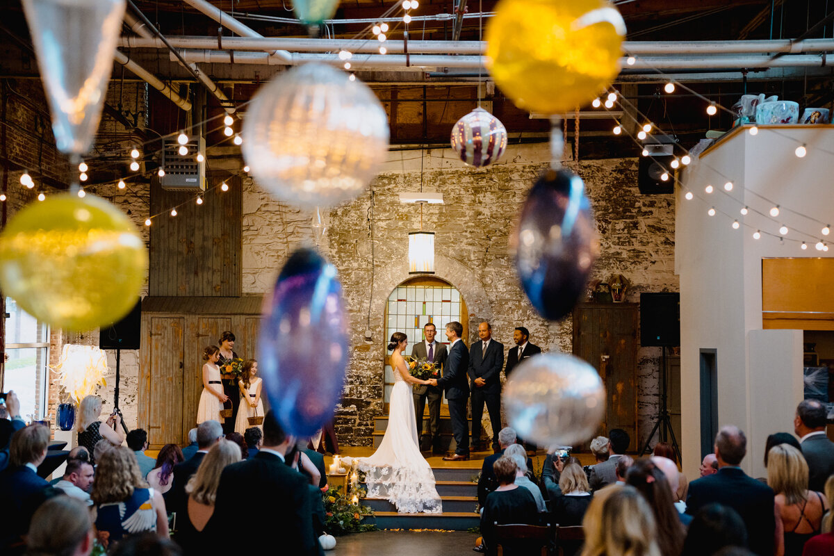 View from behind the guests of a couple standing up at their wedding as they say their vows.